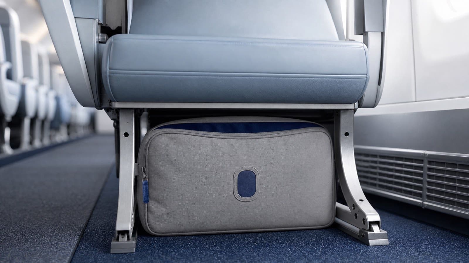A soft cabin bag pushed into the floor space beneath an aircraft seat